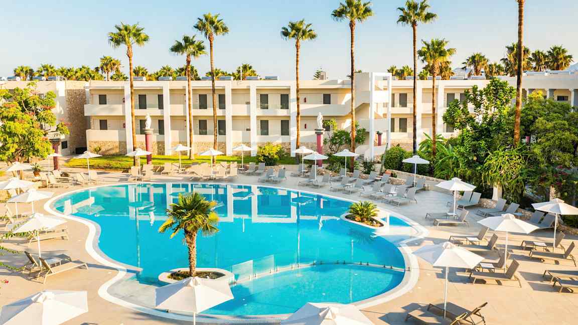 Poolområde med solsenge, parasoller og hotelbygninger i baggrunden. (AI-genereret tekst)