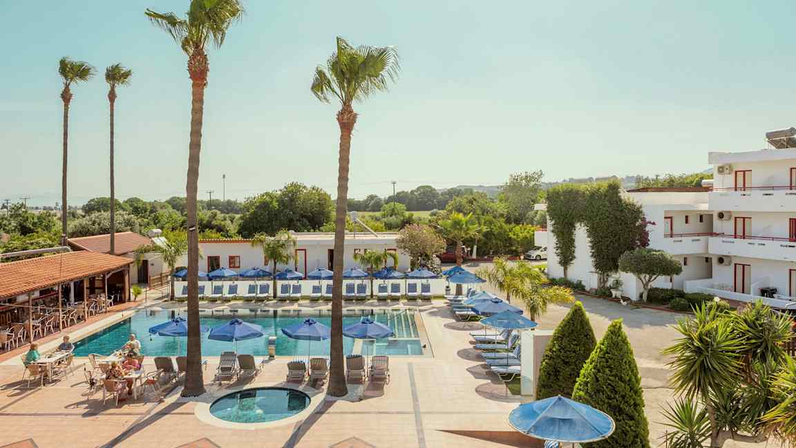 En pool med liggestole og parasoller omgivet af bygninger og træer. (AI-genereret tekst)