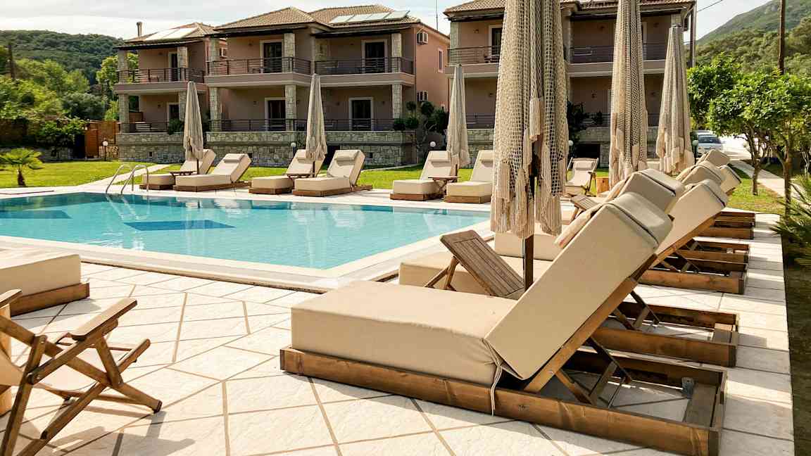 Udendørs pool med liggestole og parasoller, omgivet af bygninger og grønne områder. (AI-genereret tekst)