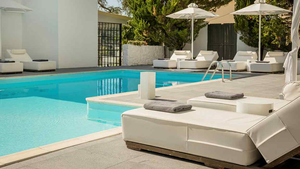 Udendørs pool med liggestole og parasoller. (AI-genereret tekst)