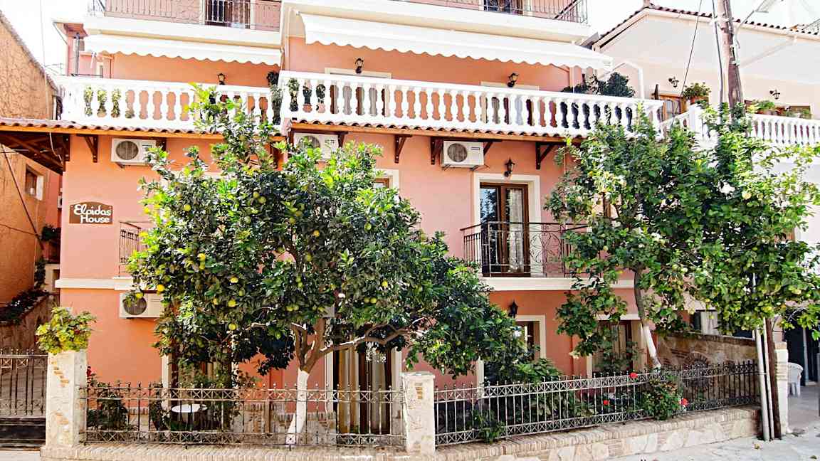 En lyserød bygning med altaner og grønne træer foran. (AI-genereret tekst)