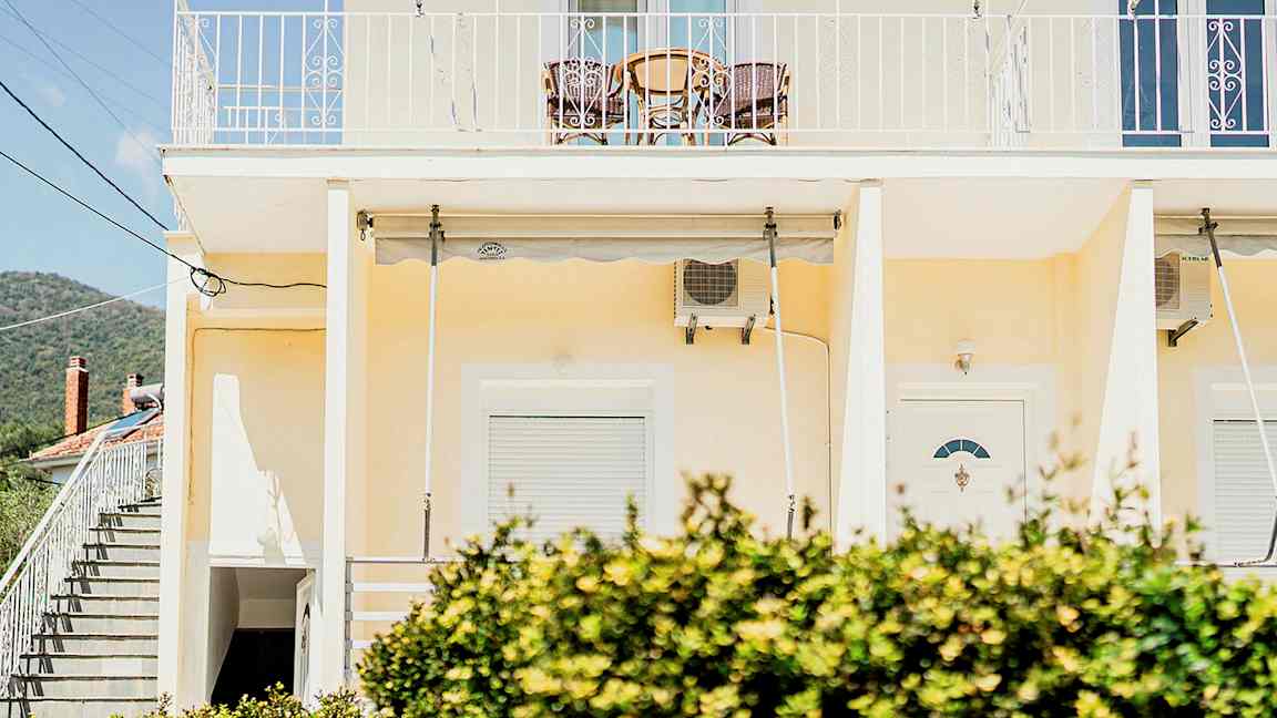 En gul bygning med en altan øverst og buske i forgrunden. (AI-genereret tekst)