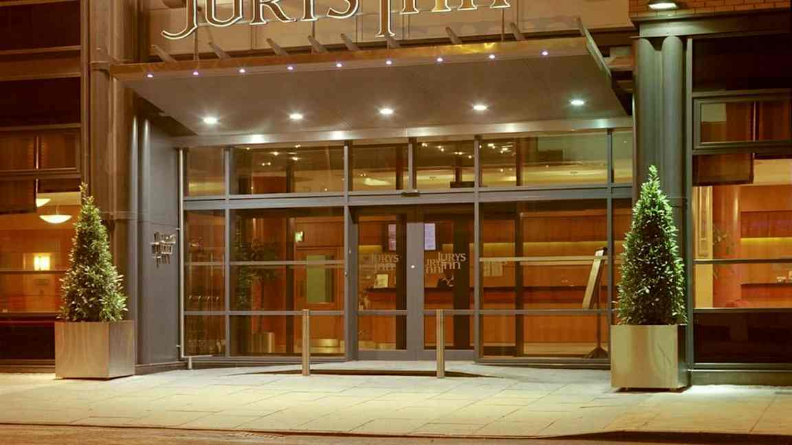 Hotelindgang med glasdøre og skiltet 'Jurys Inn' ovenfor. (AI-genereret tekst)