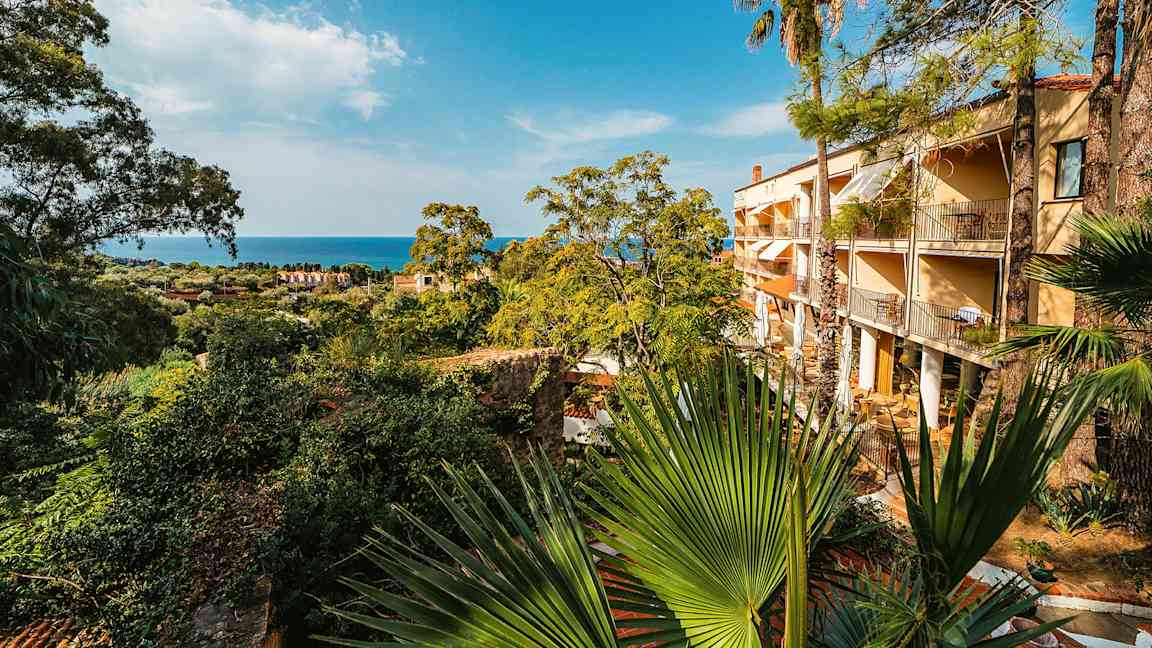 Et hotel med altaner omgivet af frodig vegetation og udsigt over havet. (AI-genereret tekst)