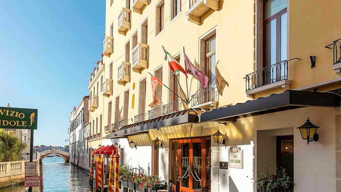 En gul bygning med altaner langs en kanal, med en gangbro i baggrunden. (AI-genereret tekst)