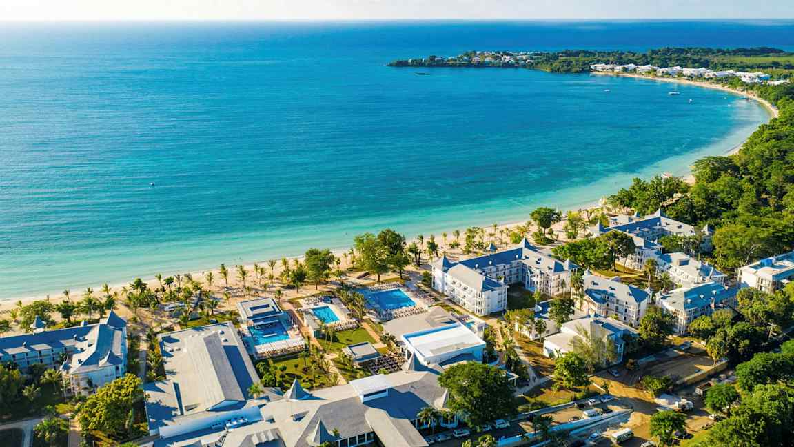 Billede af en kyststrækning med turkis vand, en hvid sandstrand og hotelbygninger i nærheden. (AI-genereret tekst)