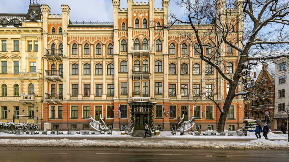 Facaden af en statelig bygning med gotisk arkitektur og mange vinduer, set om vinteren med sne på jorden. (AI-genereret tekst)
