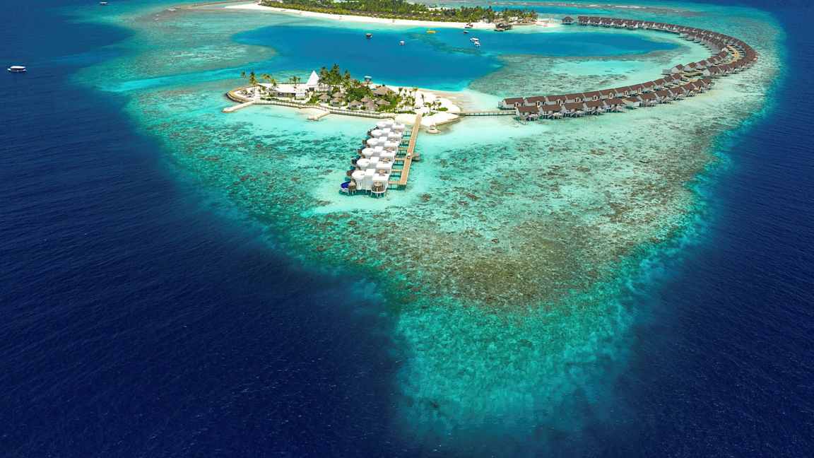 Luftfoto af en tropisk ø med overhavsbungalower og blå lagune omgivet af koralrev. (AI-genereret tekst)