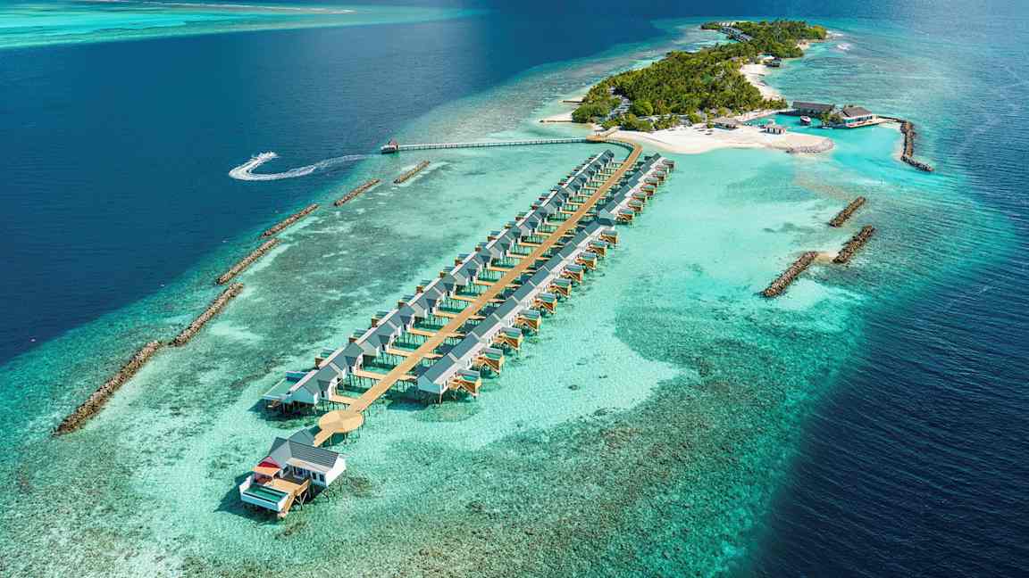 Luftfoto af en tropisk ø med strandvillaer i vandet og omgivet af turkis hav. (AI-genereret tekst)