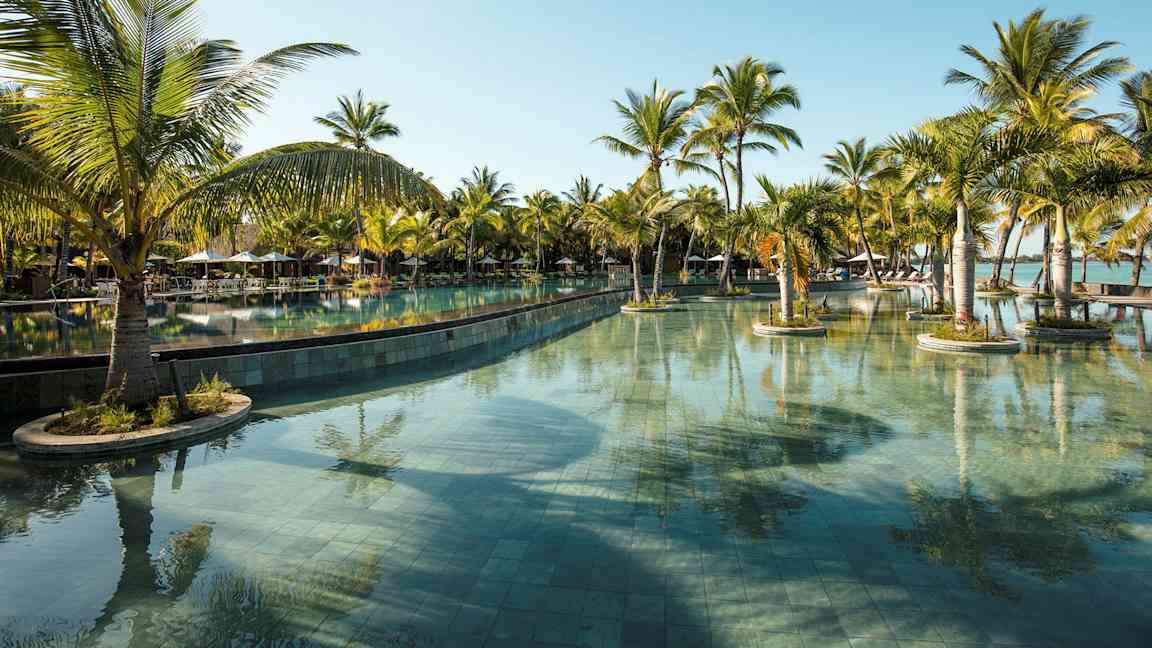 En stor swimmingpool omgivet af palmer under en klar blå himmel. (AI-genereret tekst)