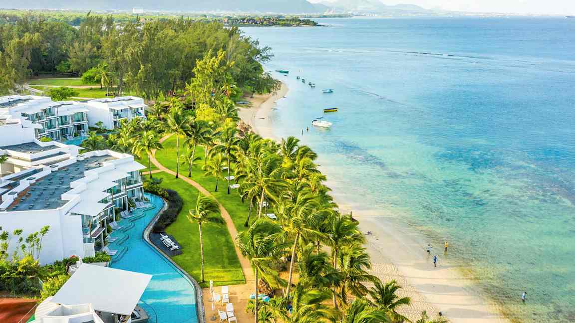 Et kystlandskab med hvide bygninger, palmer, sandstrand og turkis hav. (AI-genereret tekst)