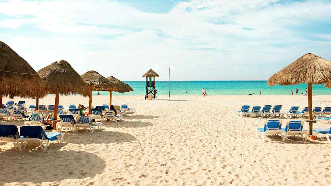 En sandstrand med liggestole og parasoller samt havet i baggrunden. (AI-genereret tekst)