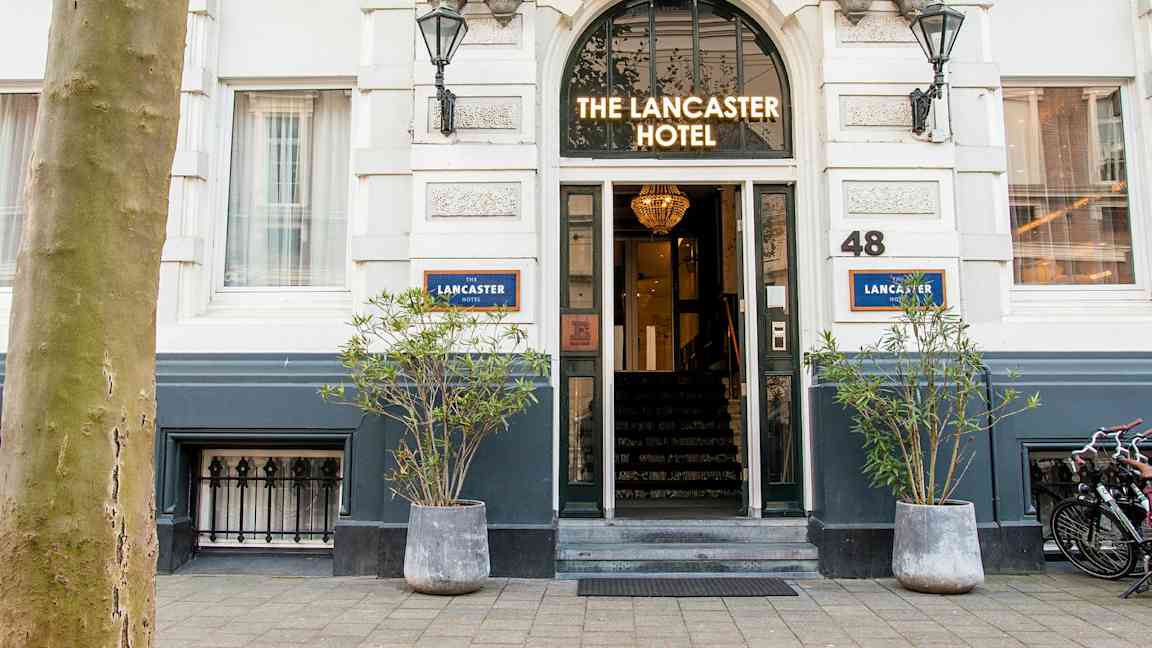 Indgang til et hotel med skiltet 'The Lancaster Hotel' over døren. (AI-genereret tekst)
