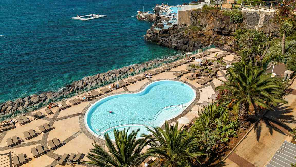 Lukket pool med liggestole og udsigt over havet. (AI-genereret tekst)