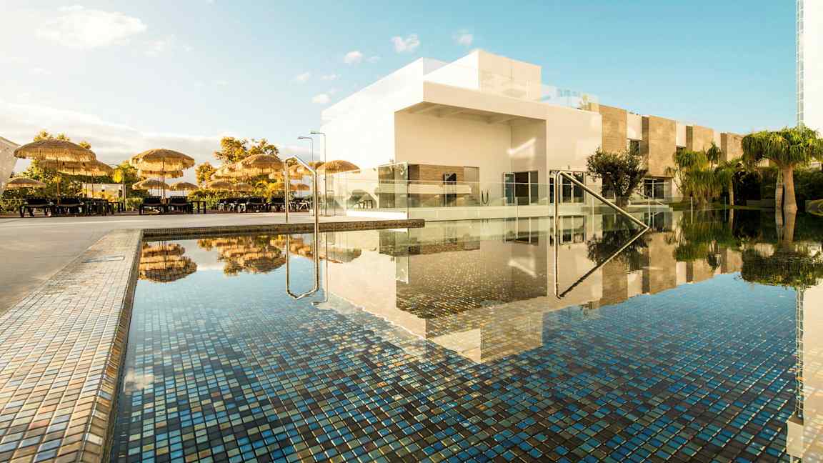 Poolområde med parasoller og hvide bygninger. (AI-genereret tekst)