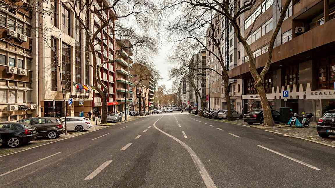 Et billede af en tom bygade omgivet af bygninger og træer. (AI-genereret tekst)