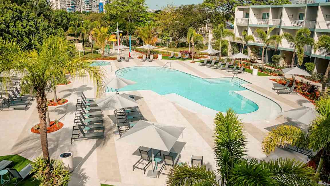 Udendørs pool med liggestole og parasoller, omgivet af træer og grønne planter. (AI-genereret tekst)