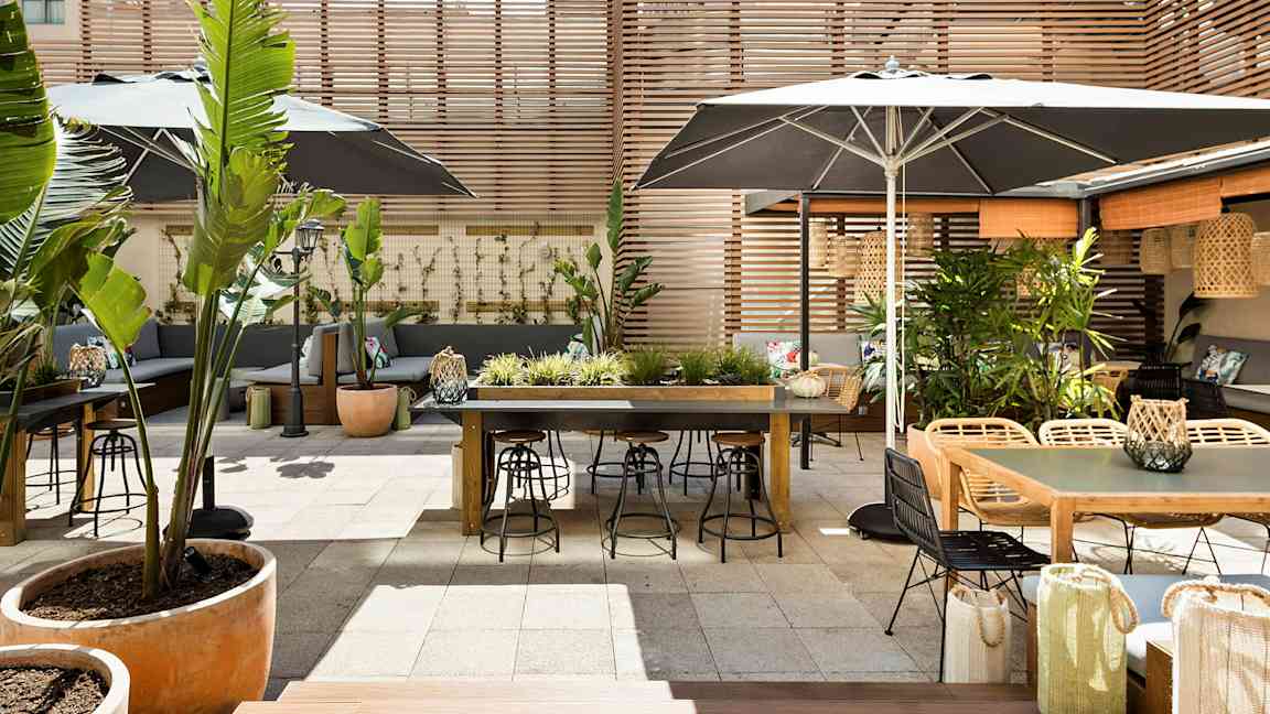 En udendørs terrasse med borde, stole og plantepynt, omgivet af træpaneler. (AI-genereret tekst)