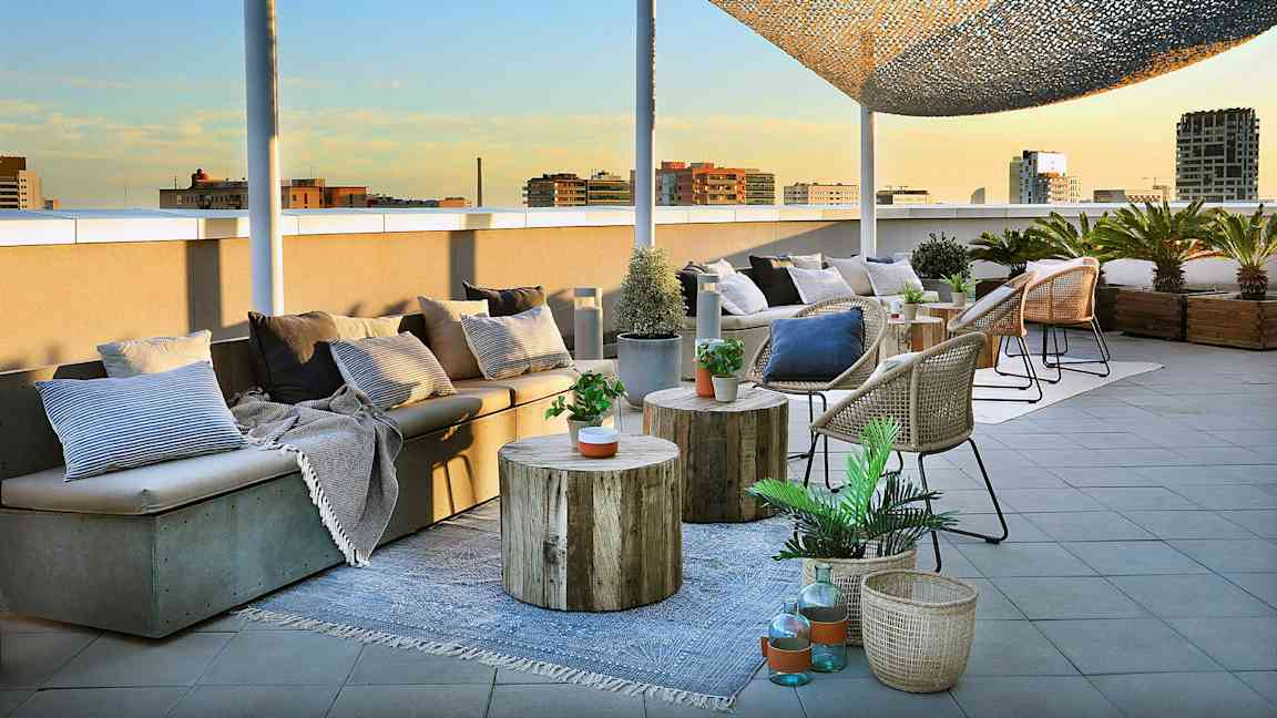 En tagterrasse med siddepladser, borde og kurve dekoreret med planter og puder er afbildet. (AI-genereret tekst)