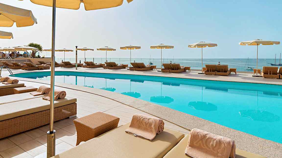 Liggestole med parasoller omkring en pool, og udsigt over havet. (AI-genereret tekst)