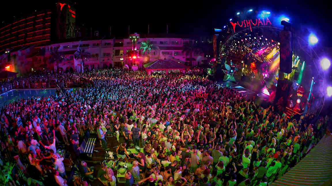 En natklub med et publikum foran en farverigt oplyst scene. (AI-genereret tekst)