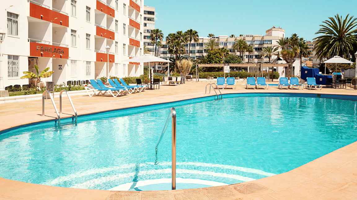 En udendørs pool med liggestole ved et hotel. (AI-genereret tekst)