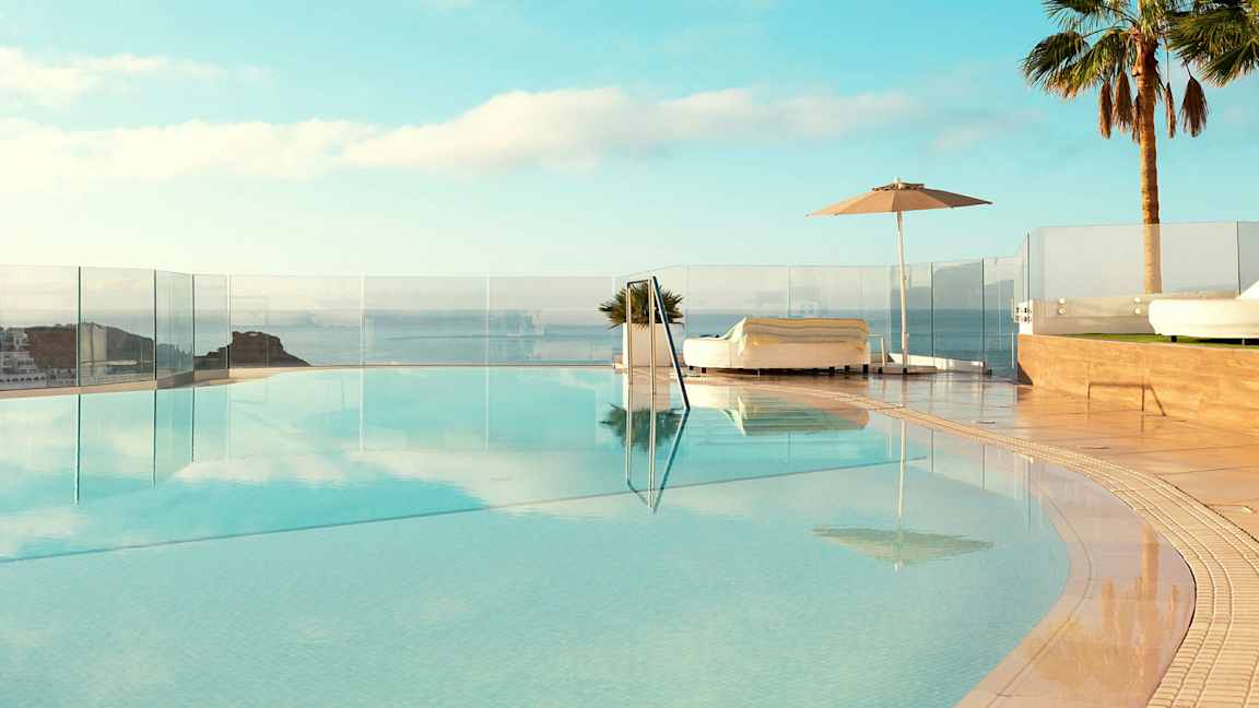 En infinitypool med udsigt over havet, omgivet af liggestole og palmer. (AI-genereret tekst)