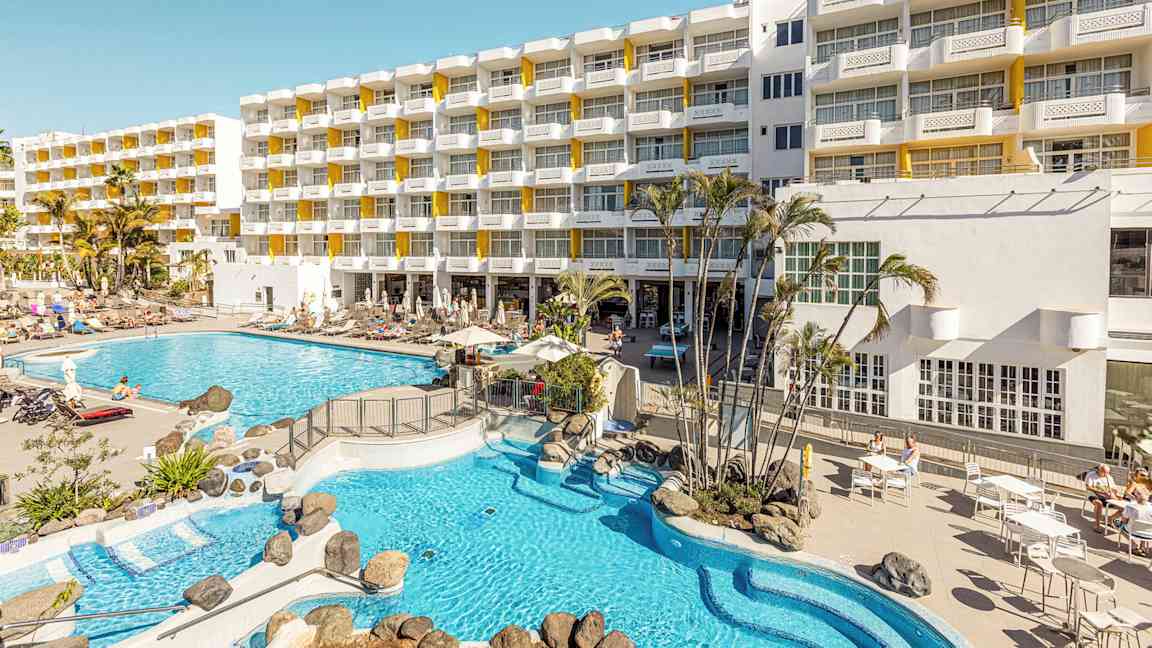 Hotelbygning med liggestole og poolområde. (AI-genereret tekst)