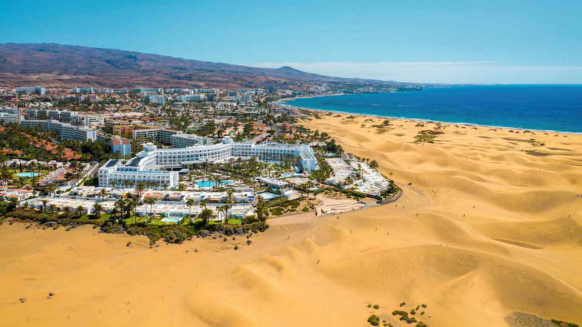 Luftfoto af et hotelområde ved store sandklitter og havet. (AI-genereret tekst)