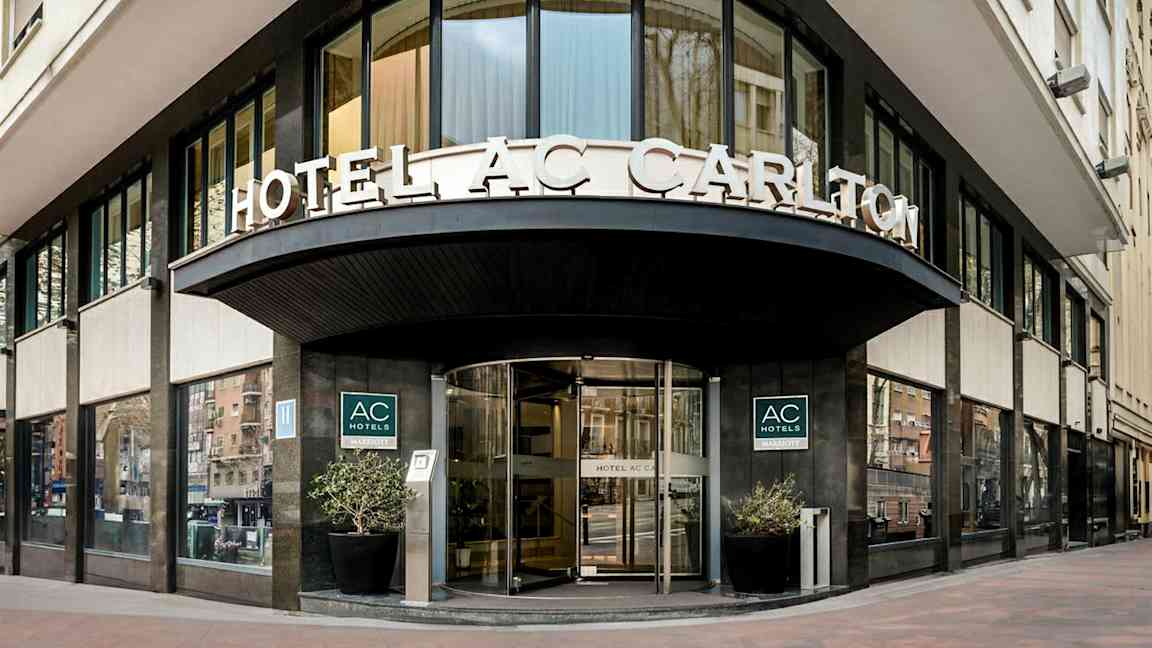 En hotelfacade med skilteteksten "HOTEL AC CARLTON" synlig over indgangen. (AI-genereret tekst)