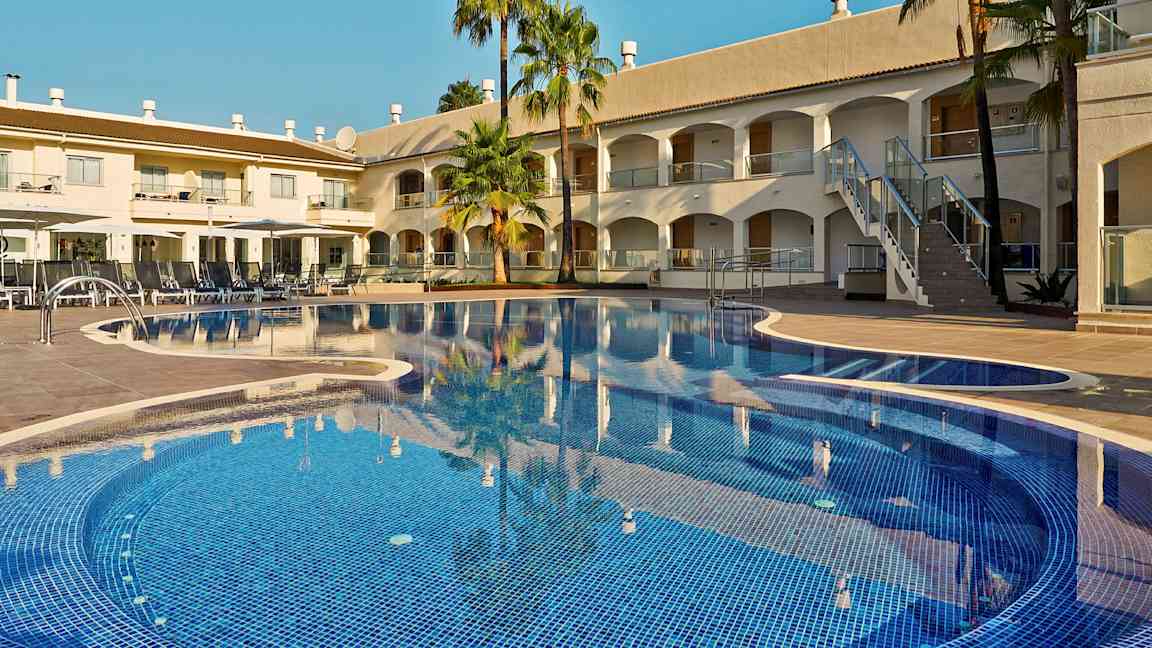 Billede af en hotelpool med liggestole og bygninger i baggrunden. (AI-genereret tekst)