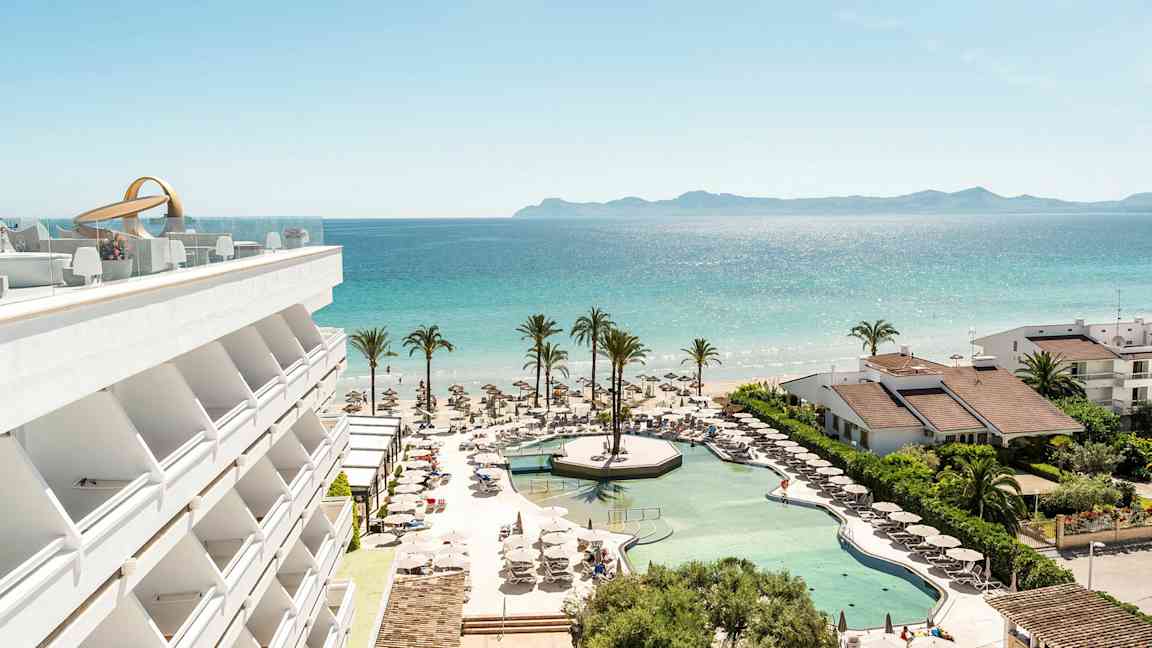 En udsigt over hotelpool, strand og hav med palmer og bygninger. (AI-genereret tekst)