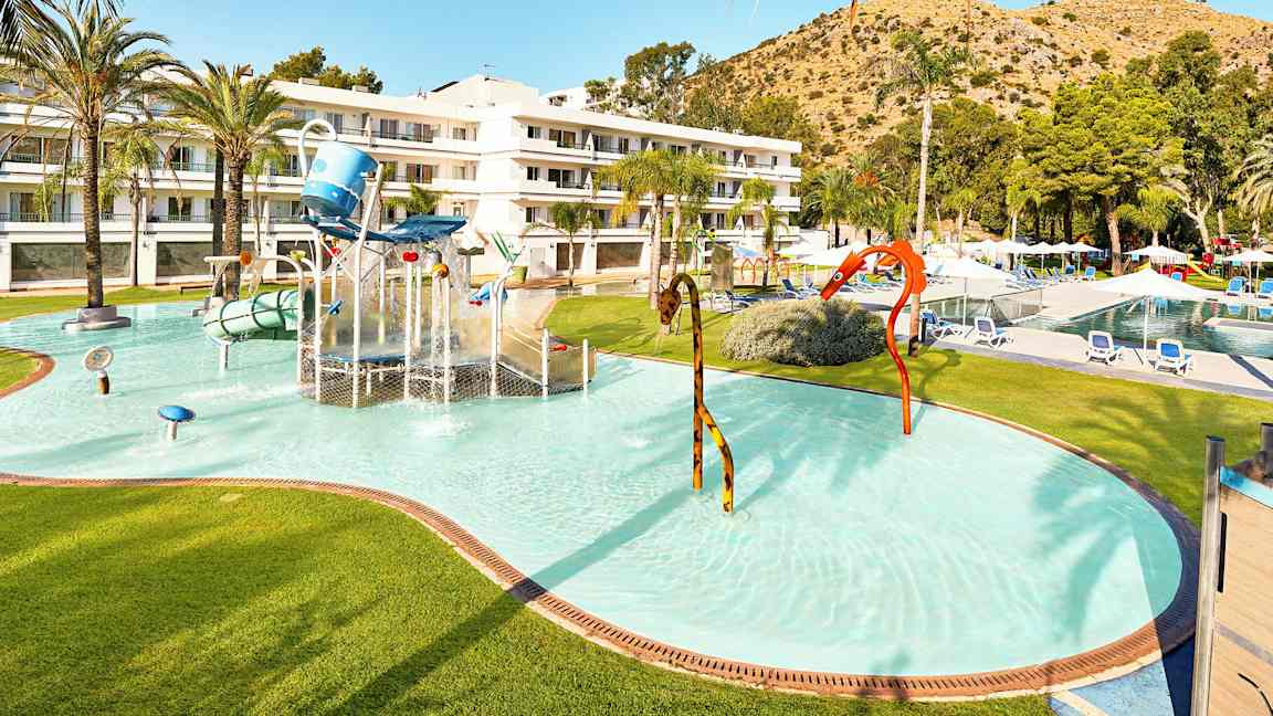 Børnepool med vandleg og hotelbygning i baggrunden. (AI-genereret tekst)
