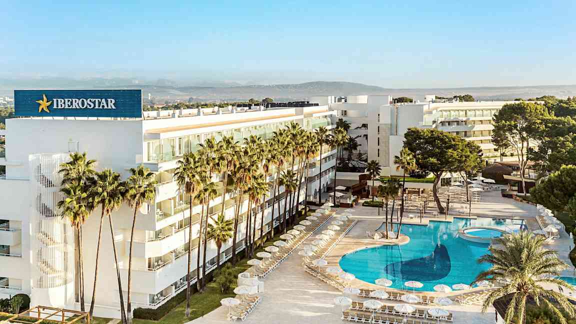 Et moderne hotel omgivet af palmer med en stor, klarblå pool. (AI-genereret tekst)