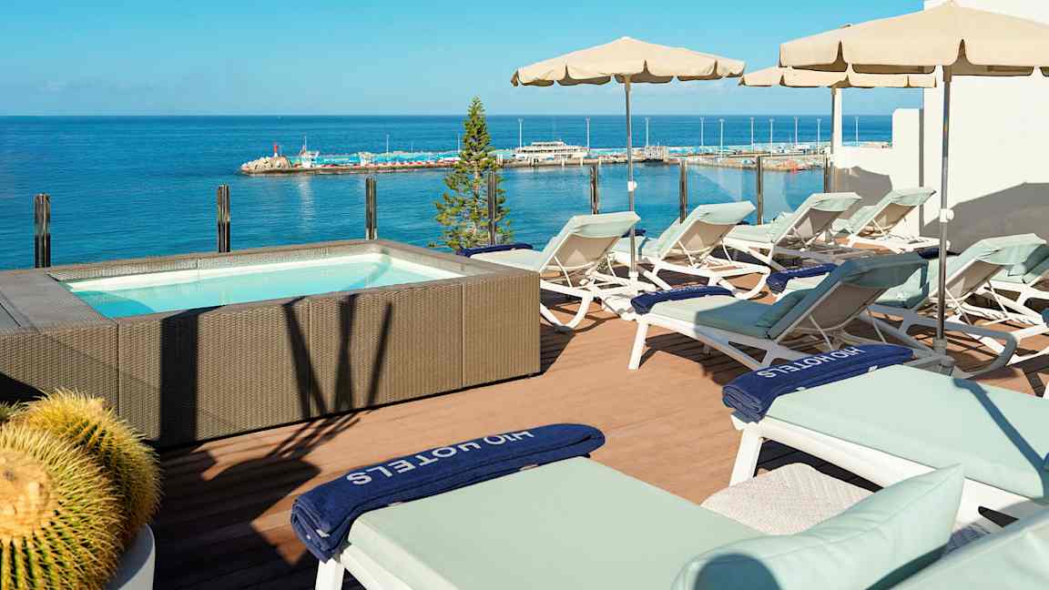 Terrasse med liggestole og parasoller ved et boblebad med havudsigt. (AI-genereret tekst)