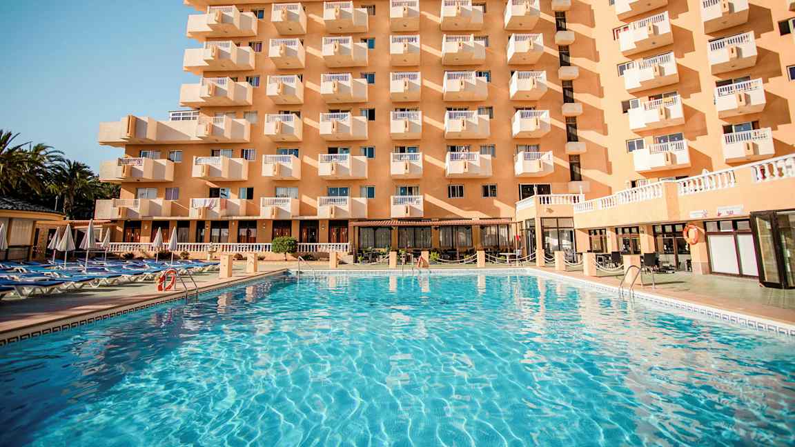 Bygning med flere altaner og en stor pool foran. (AI-genereret tekst)