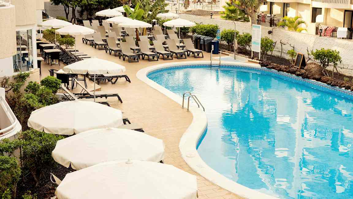 Poolområde med liggestole og parasoller ved et hotel. (AI-genereret tekst)