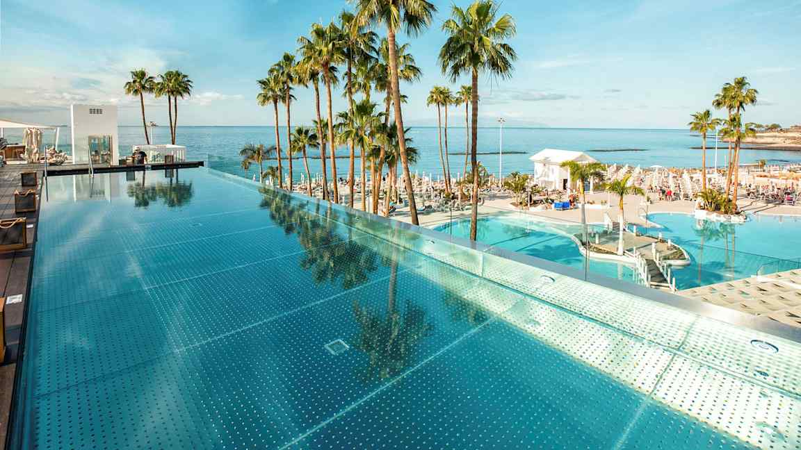 En infinitypool ved havet omgivet af palmer. (AI-genereret tekst)