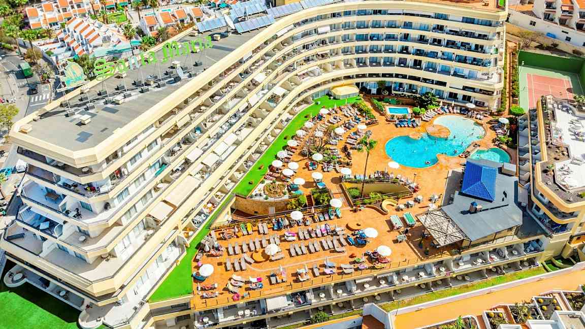 Billede af et hotel med poolområde og omkringliggende ferieboliger. (AI-genereret tekst)