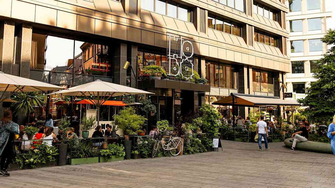 En udendørs servering foran en moderne bygning med store glasvinduer. (AI-genereret tekst)