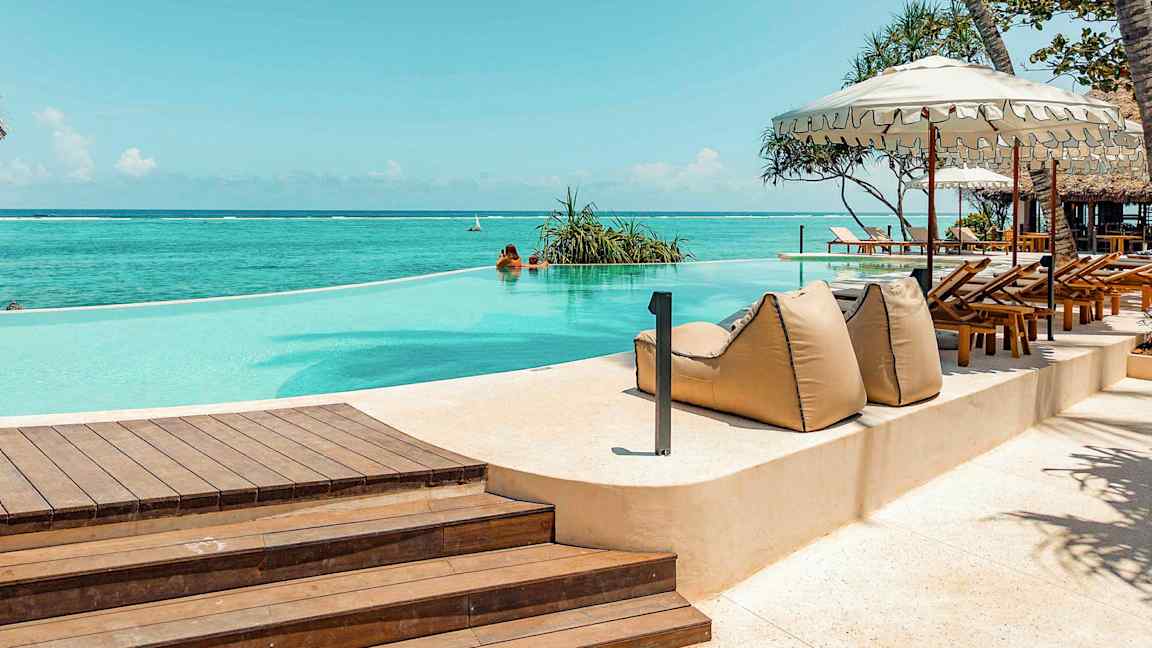 En infinity-pool ved havet, omgivet af liggestole og parasoller. (AI-genereret tekst)