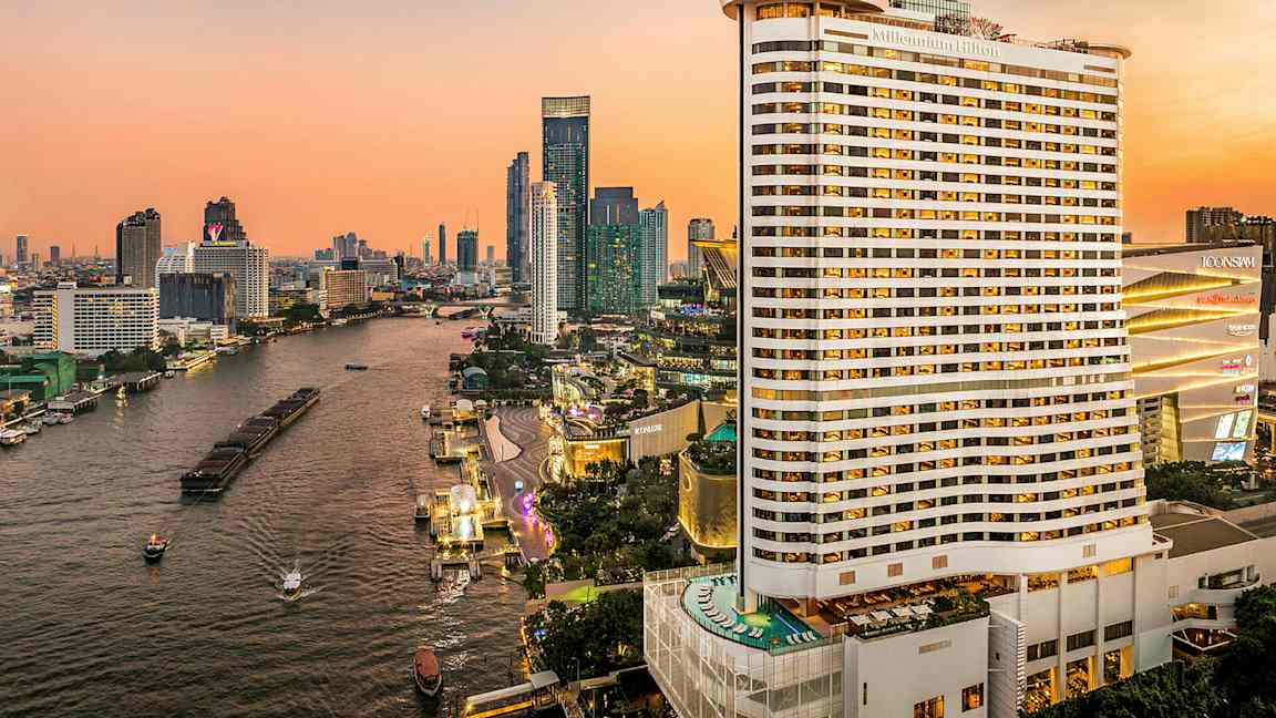 Udsigt over en flod omgivet af høje bygninger under en solnedgang. Et stort hotel er synligt i forgrunden. (AI-genereret tekst)