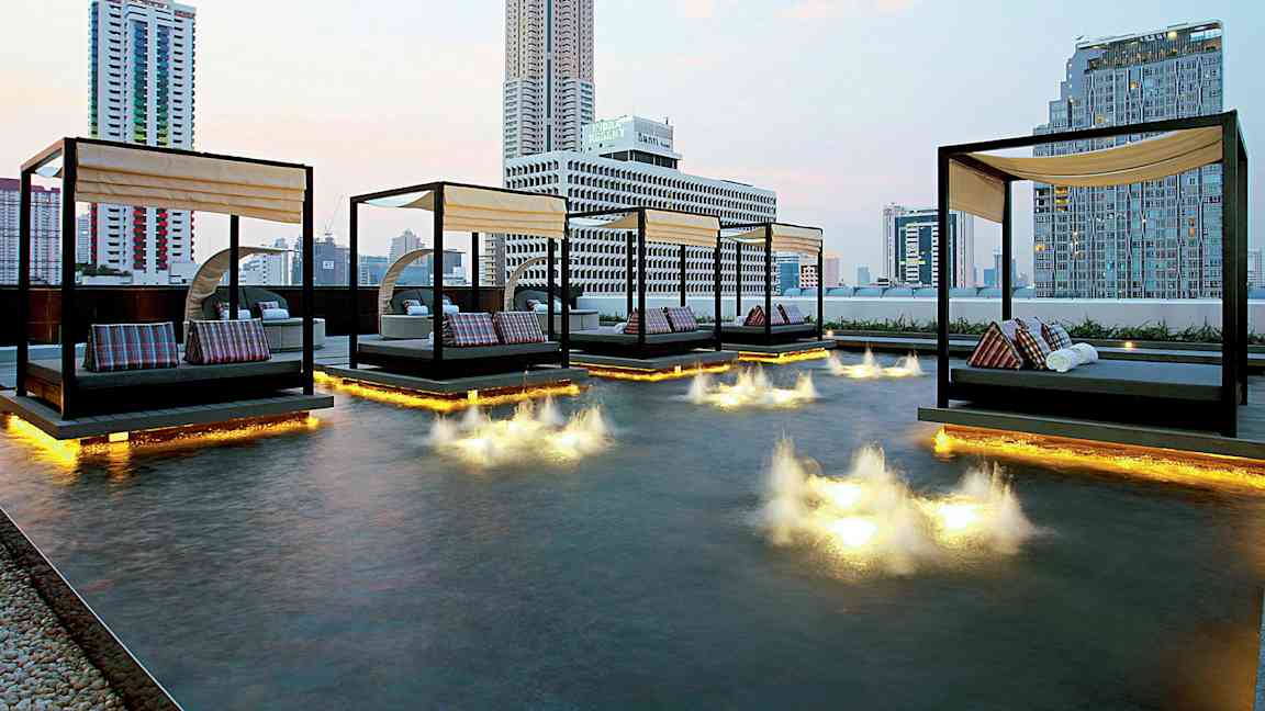 Billede af en moderne byudsigt med dagsenge placeret over en lav pool med lysinstallationer i vandet. (AI-genereret tekst)