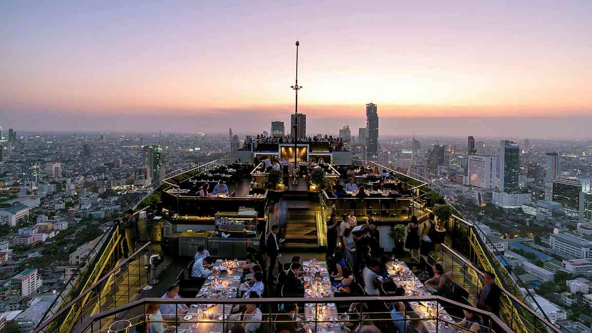 Tagterrasse ved solnedgang med restaurantgæster og panoramaudsigt over byens skyline. (AI-genereret tekst)