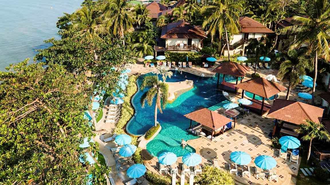 Et feriested med pool, palmer og parasoller ved havet. (AI-genereret tekst)