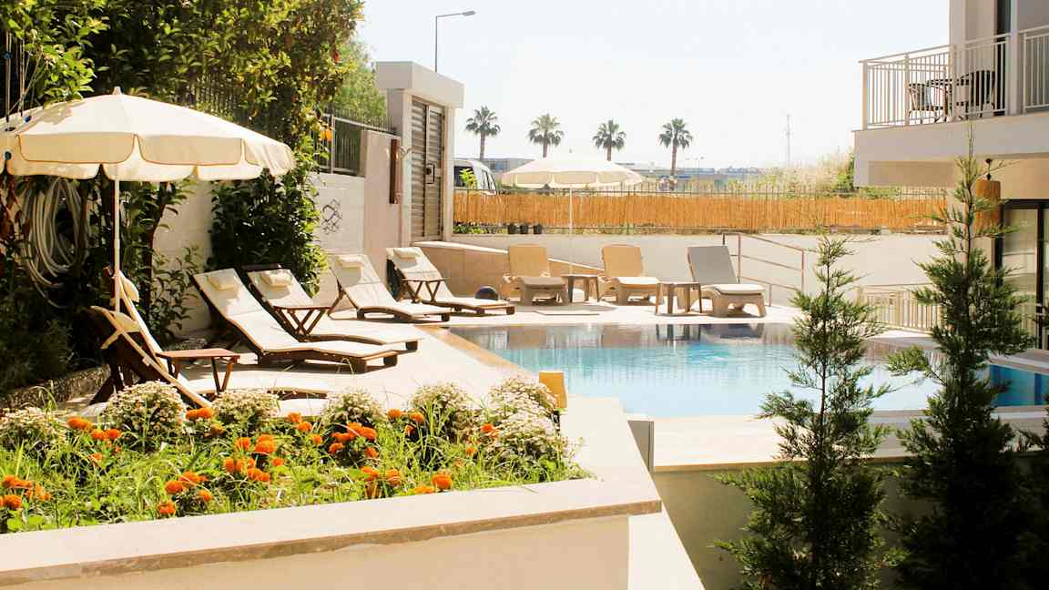 En pool omgivet af liggestole, parasoller og grønne omgivelser. (AI-genereret tekst)