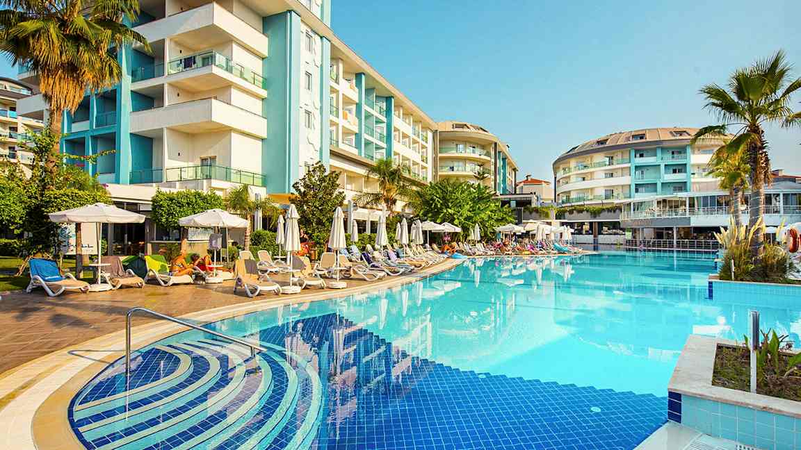 Hotel bygget omkring en udendørs pool med liggestole og parasoller. (AI-genereret tekst)