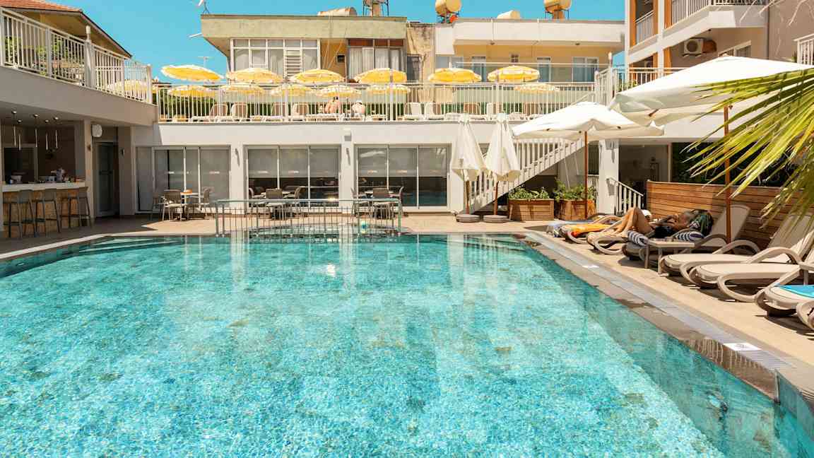 En udendørs pool omgivet af liggestole og parasoller på et hotel. (AI-genereret tekst)