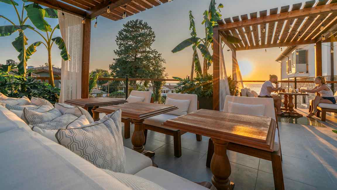 Udendørs område med træpergola, siddepladser og udsigt ved solnedgang. (AI-genereret tekst)