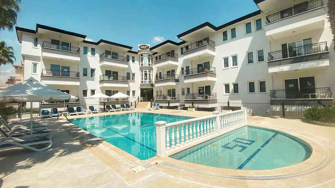 En lejlighedsbygning med altaner ud mod et poolområde. (AI-genereret tekst)